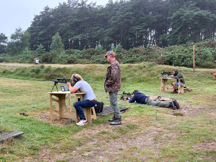 A member at a bench with another standing by, and a third shooting prone